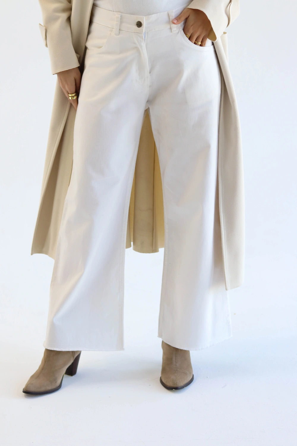 Woman wearing a beige trench coat, white pants, and brown boots on a white background