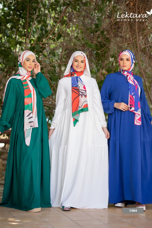 Three models wearing long modest dresses in green, white, and royal blue colors, standing together outdoors in daylight.