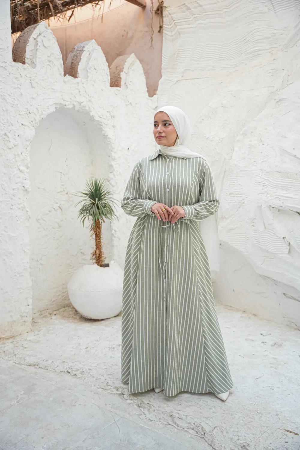 Sage green modest button dress, full-length long sleeve silhouette near white textured wall