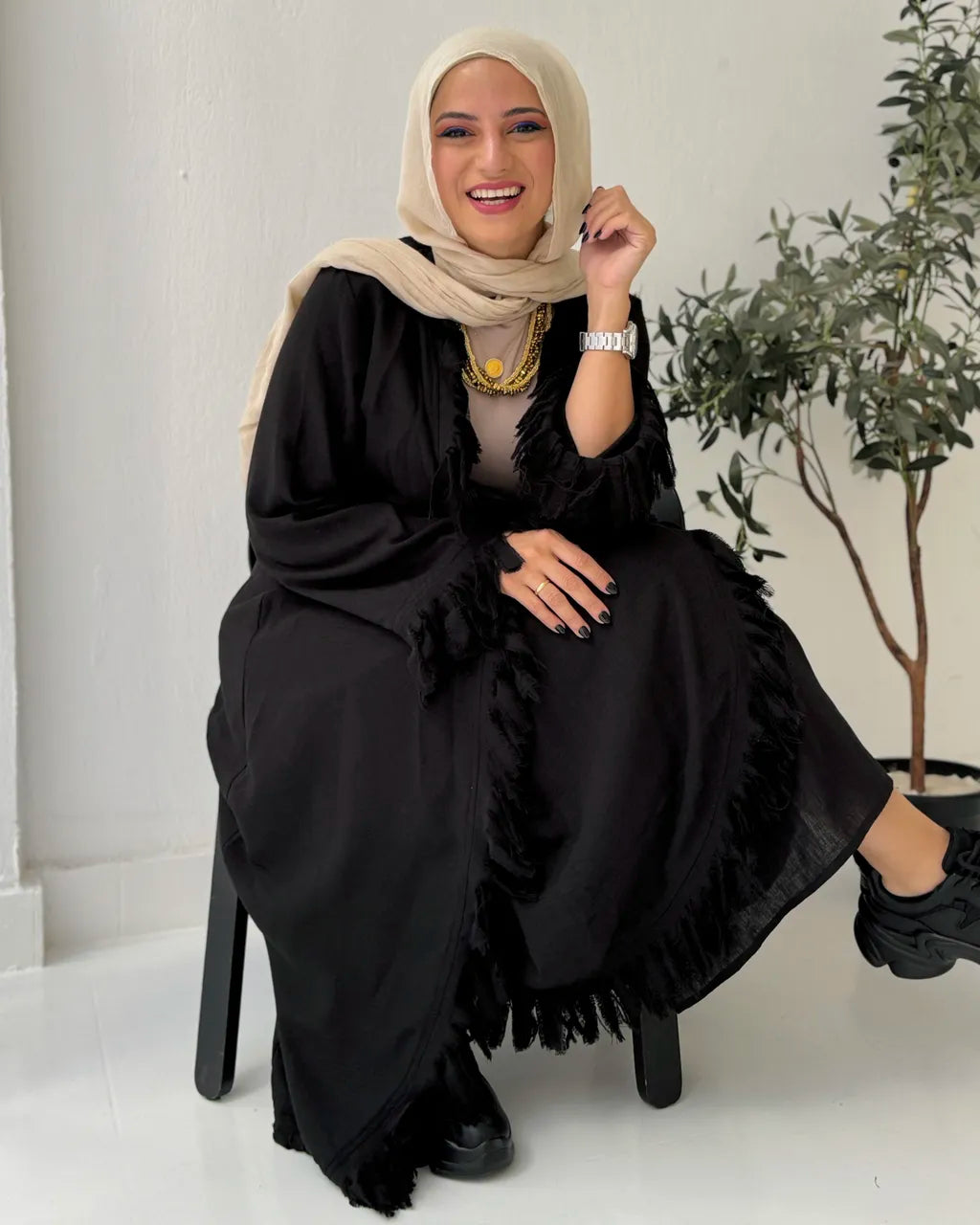 Woman wearing a black set with ruffled details, sitting on a white floor with a plant in the background.