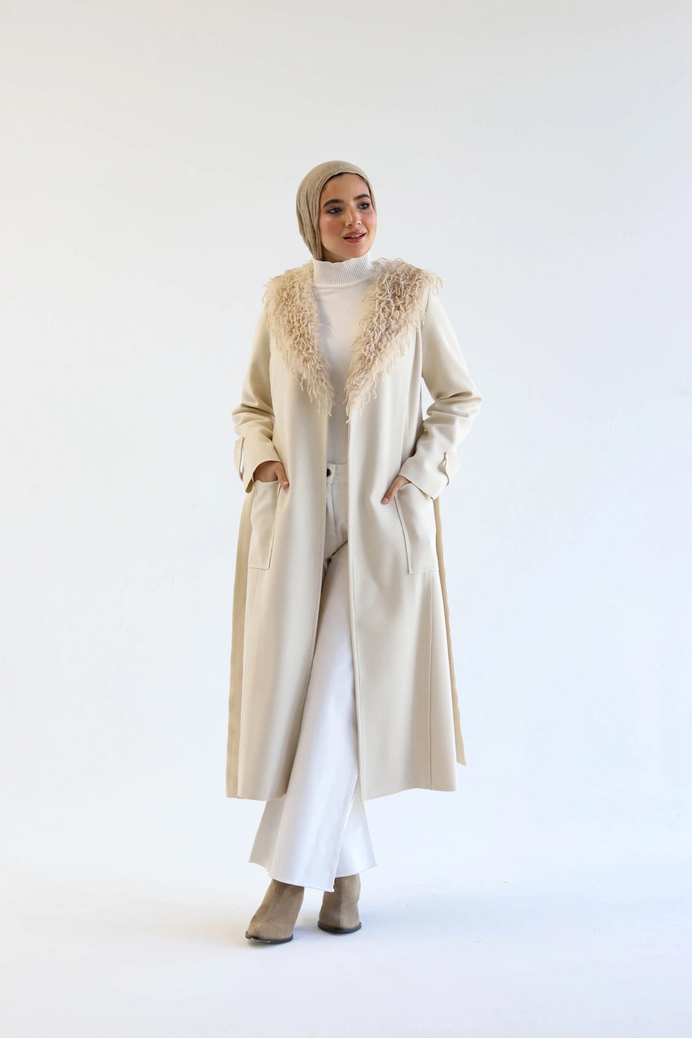 Woman wearing a long beige coat with fur trim on a white background