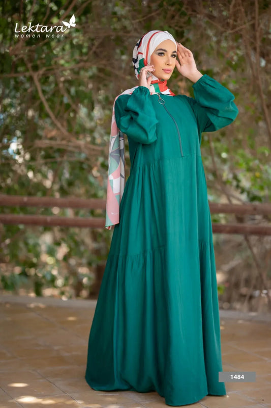 Full-length modest maxi dress in deep green color worn by one model, long sleeves and flowing silhouette, photographed outdoors near greenery.