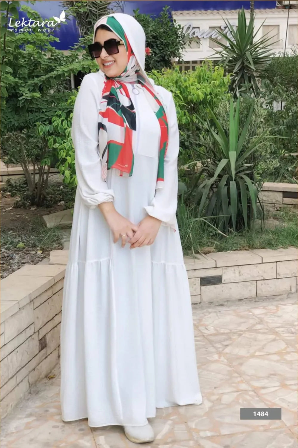 Single model wearing a white long modest dress with loose fit and full sleeves, standing on a stone walkway in natural light.