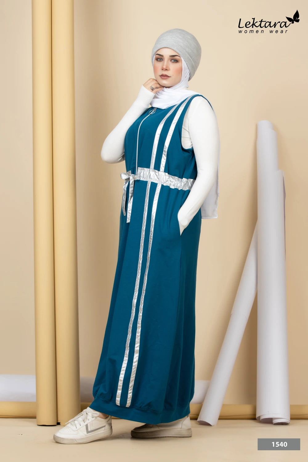 Woman wearing a teal Melton A-Line Maxi Dress with white stripes and a white hijab against a beige wall.