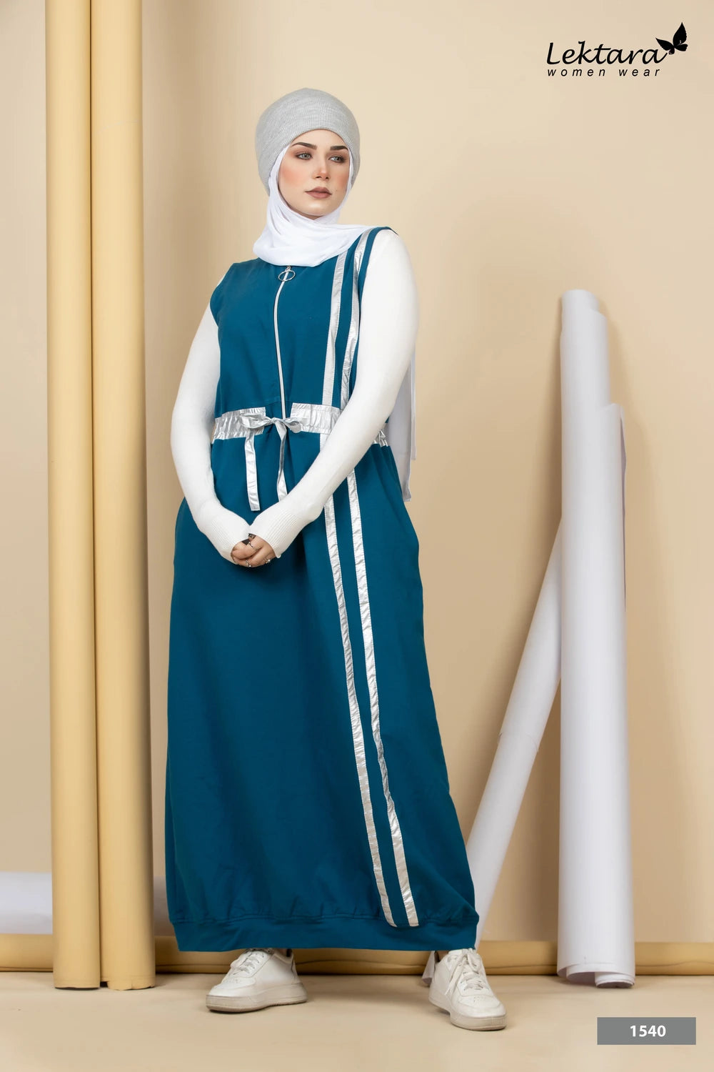 Woman wearing a teal Melton A-Line Maxi Dress with white stripes and a white hijab against a beige wall.