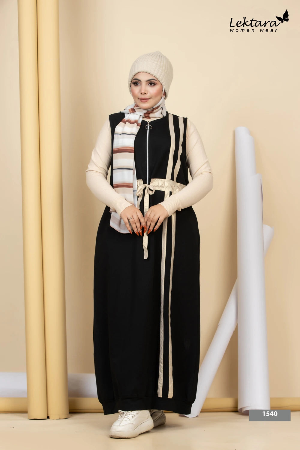Woman wearing a black Melton A-Line Maxi Dress with a striped scarf, standing against a beige wall.