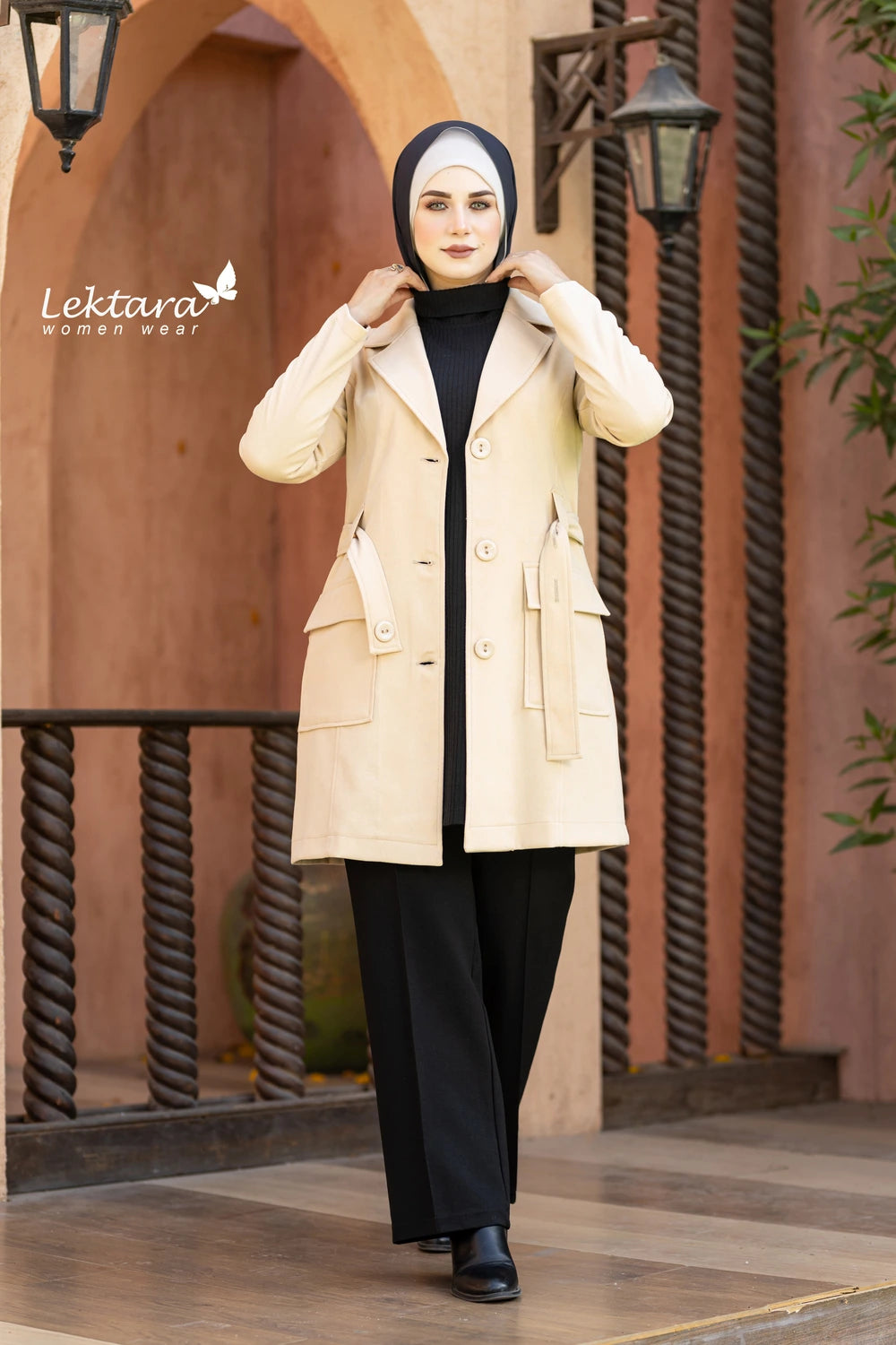 Woman wearing a beige Structured Wool Belted Jacket and black hijab standing in front of a decorative archway.