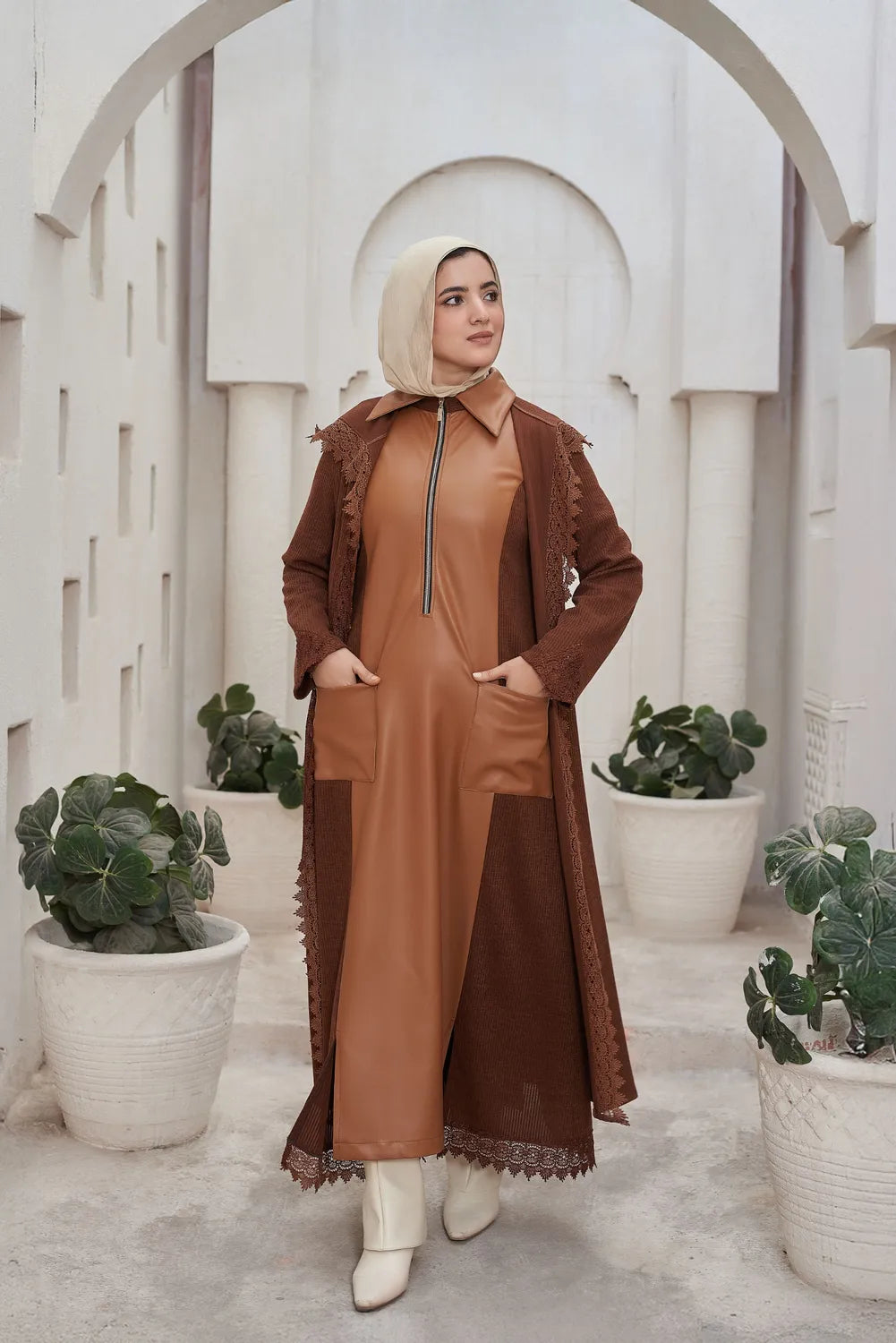 Woman in a brown Leather Dress standing in a decorative archway with plants.