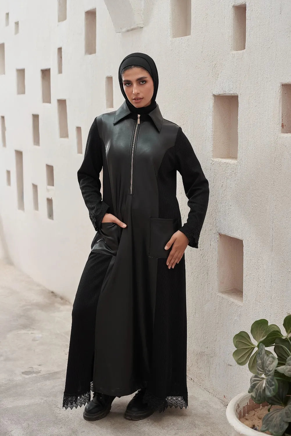 Women  wearing a black Leather Dress  with a hood in front of a textured wall.