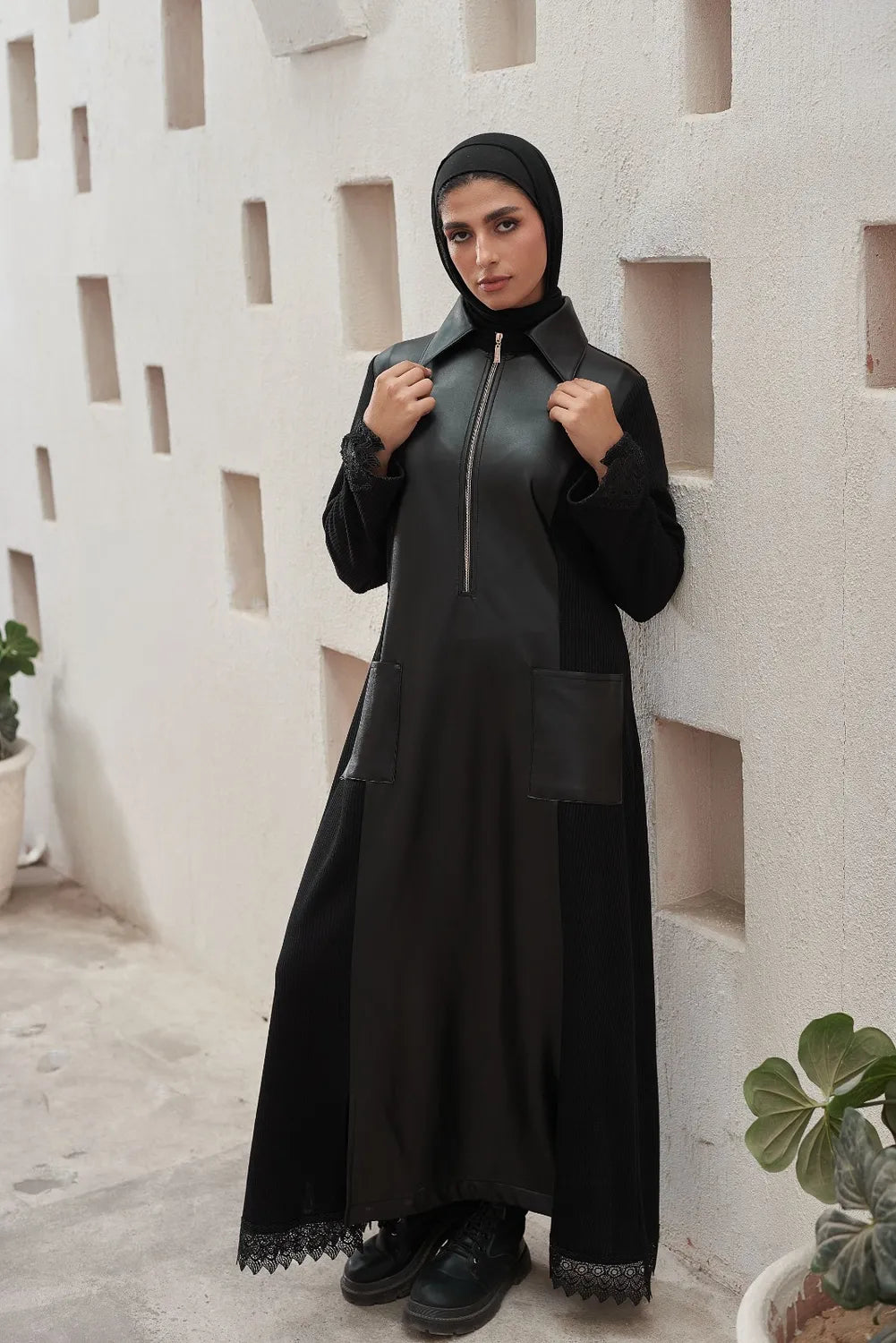 Woman wearing a black Leather Dress  in an outdoor setting with a textured wall background.