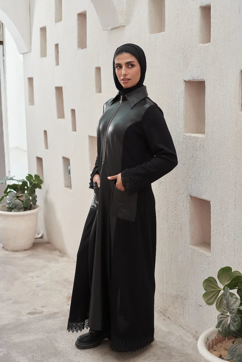 Woman in a black Elegant Dress  standing against a textured white wall.
