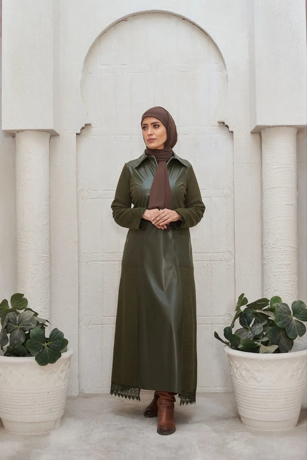 Woman in a green leather  dress standing in front of a white architectural archway with plants on either side.