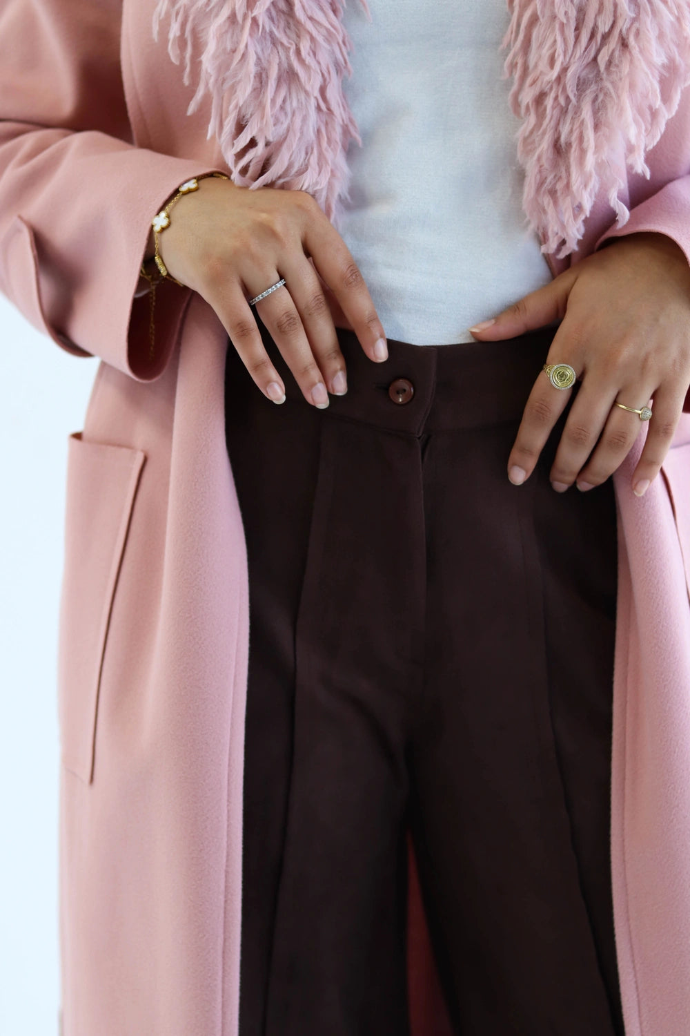 Person wearing a pink coat with a fur-lined hood, white shirt, and brown pants.