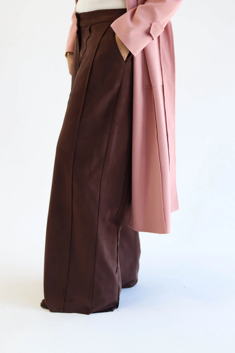 Brown wide-leg pants with a pink coat draped over them on a white background