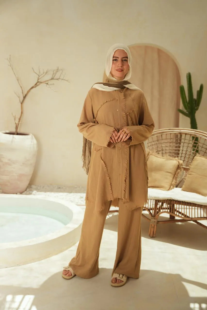Woman in a hijab  in a beige outfit standing in a room with a neutral color scheme.