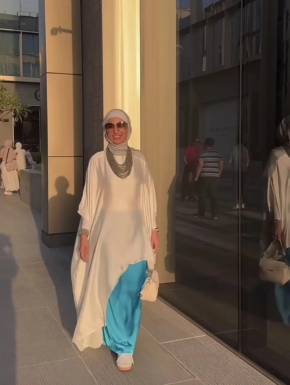 Woman in a white dress with a blue skirt standing in front of a building entrance.