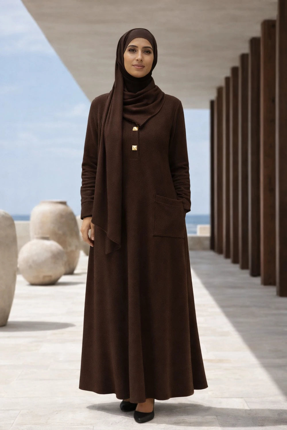 Woman wearing a brown abaya - dress in an outdoor setting with architectural elements.