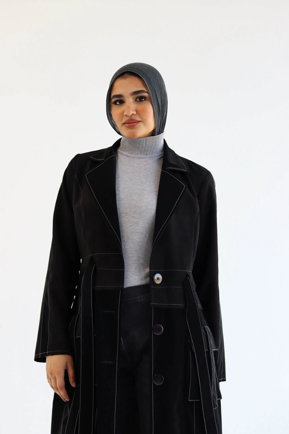 Woman wearing a black Long suede trench coat with waterproof finish styled for modest winter layering and gray turtleneck against a white background