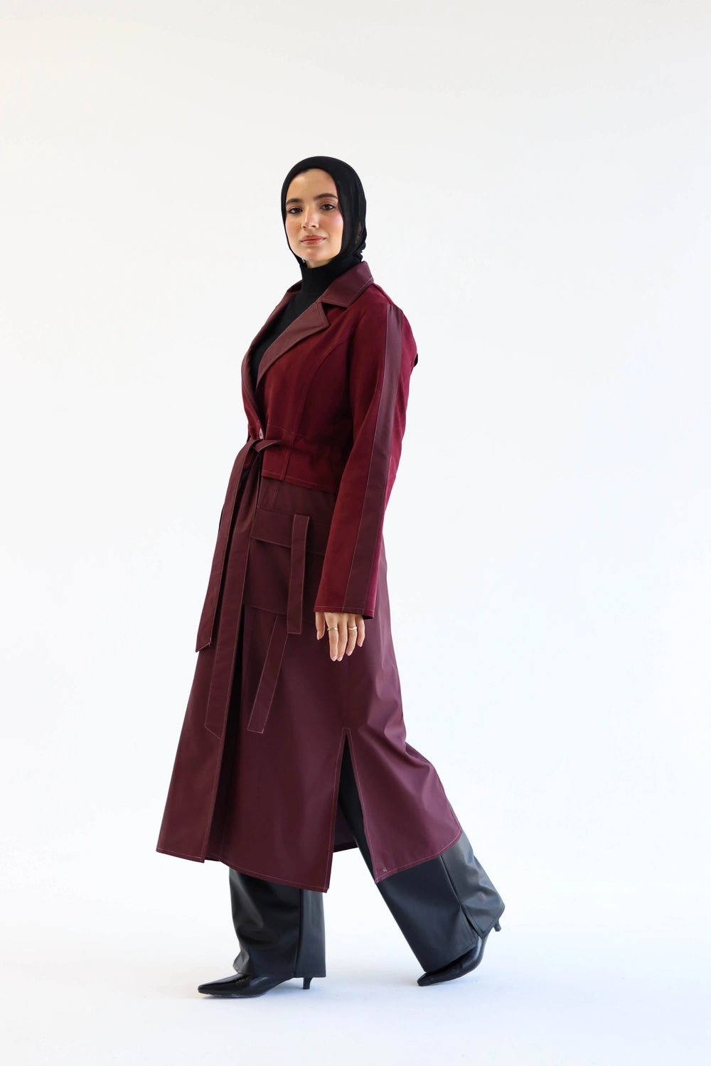 Woman wearing a long burgundy coat with a black hijab on a white background