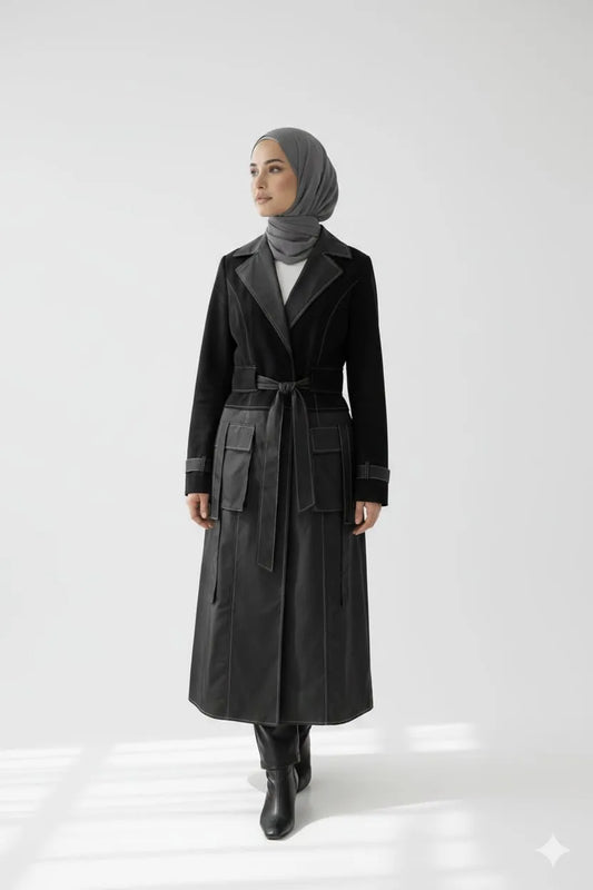 Woman in a hijab wearing a long black coat with a belt on a white background