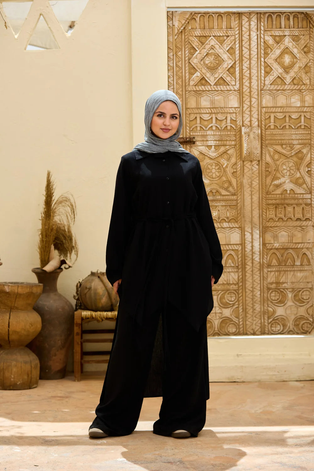 Full-length front view of the black High-Low Triangle Hem Tunic styled with wide-leg trousers
