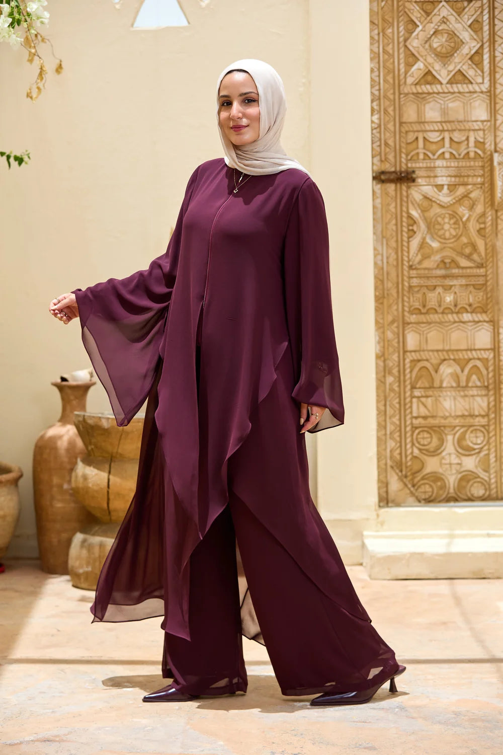 Full-length walking view of the deep purple layered chiffon tunic with an asymmetric triangle hem and wide bell sleeve