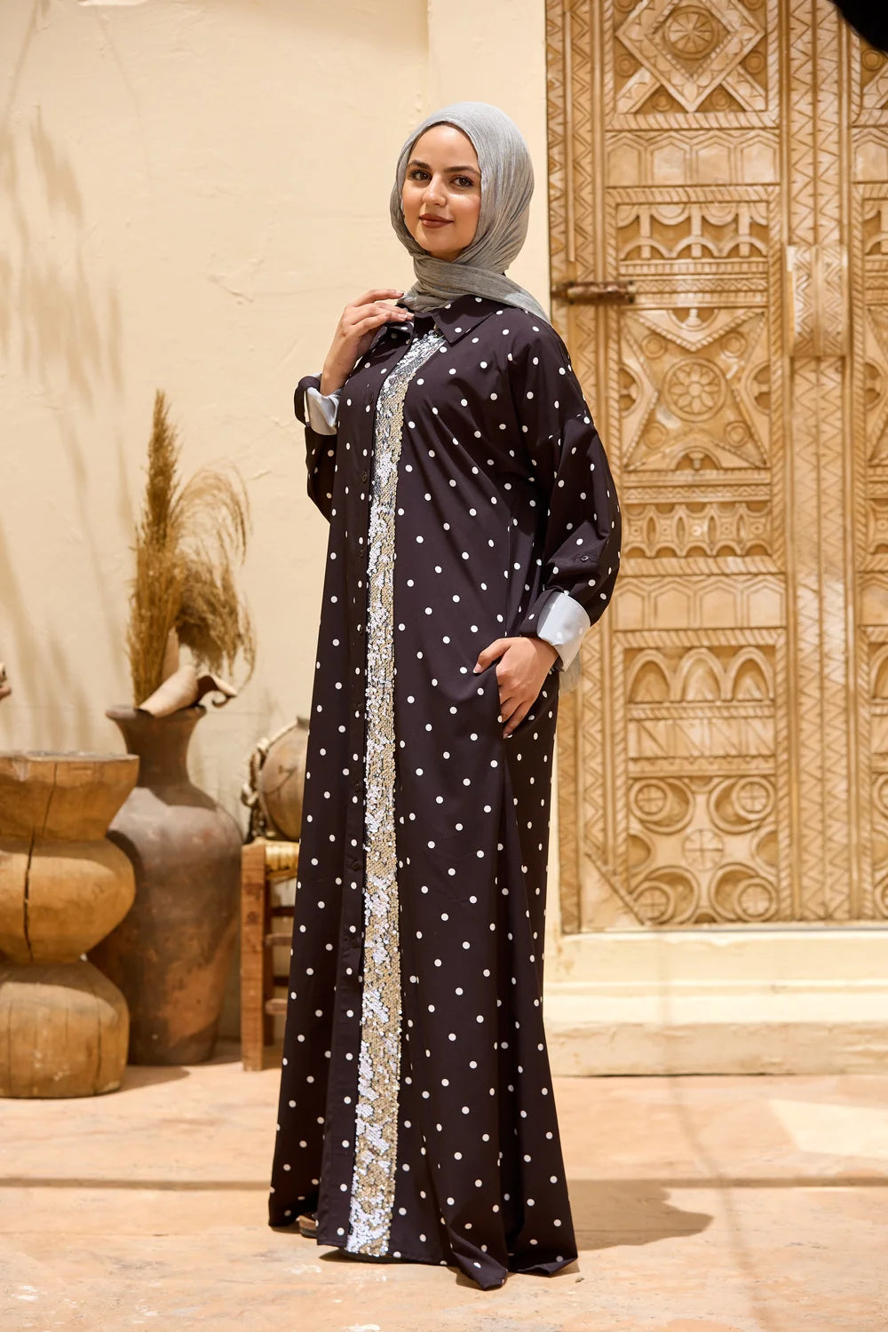 Woman wearing a black polka dot maxi shirt dress with a sequin front panel, full-length three-quarter view