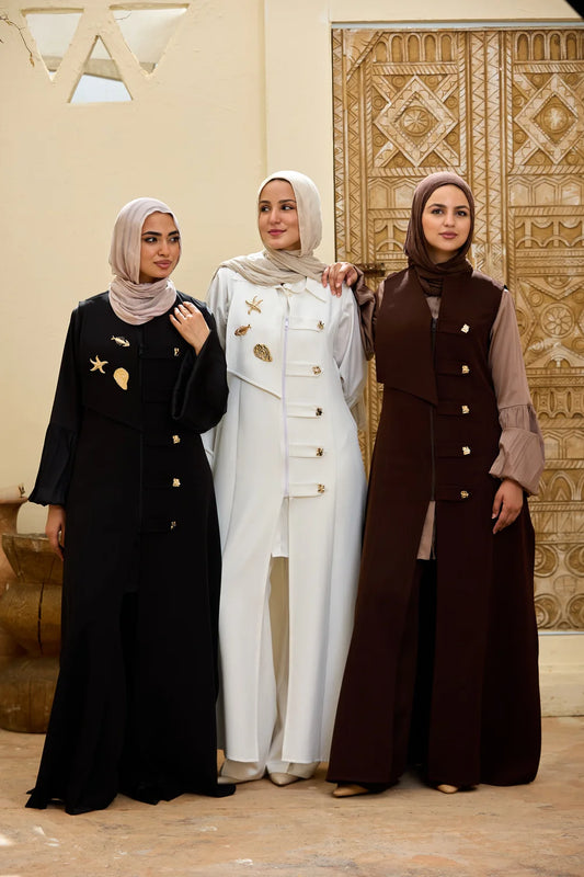 Three women wearing Longline Sleeveless Zip Vest stand together indoors. The left woman wears a black Longline Sleeveless Zip Vest with gold star and crescent moon embellishments and a light beige hijab.