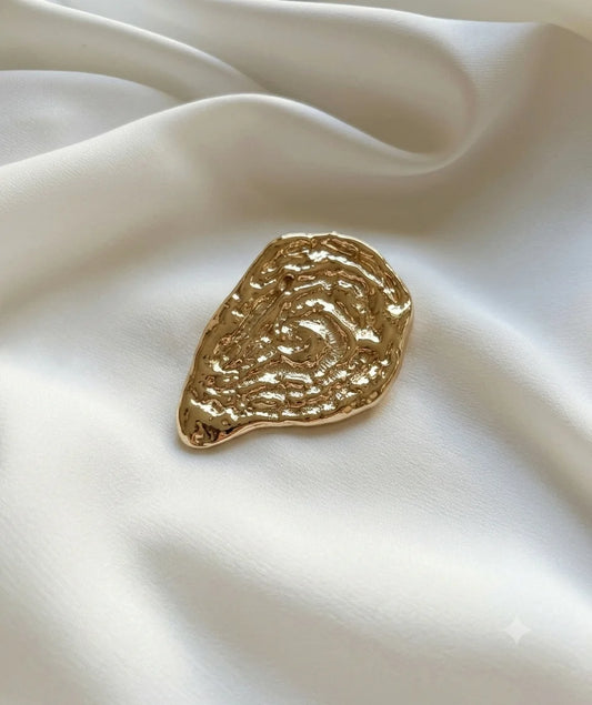 Gold-tone sculptural oyster shell brooch on ivory fabric