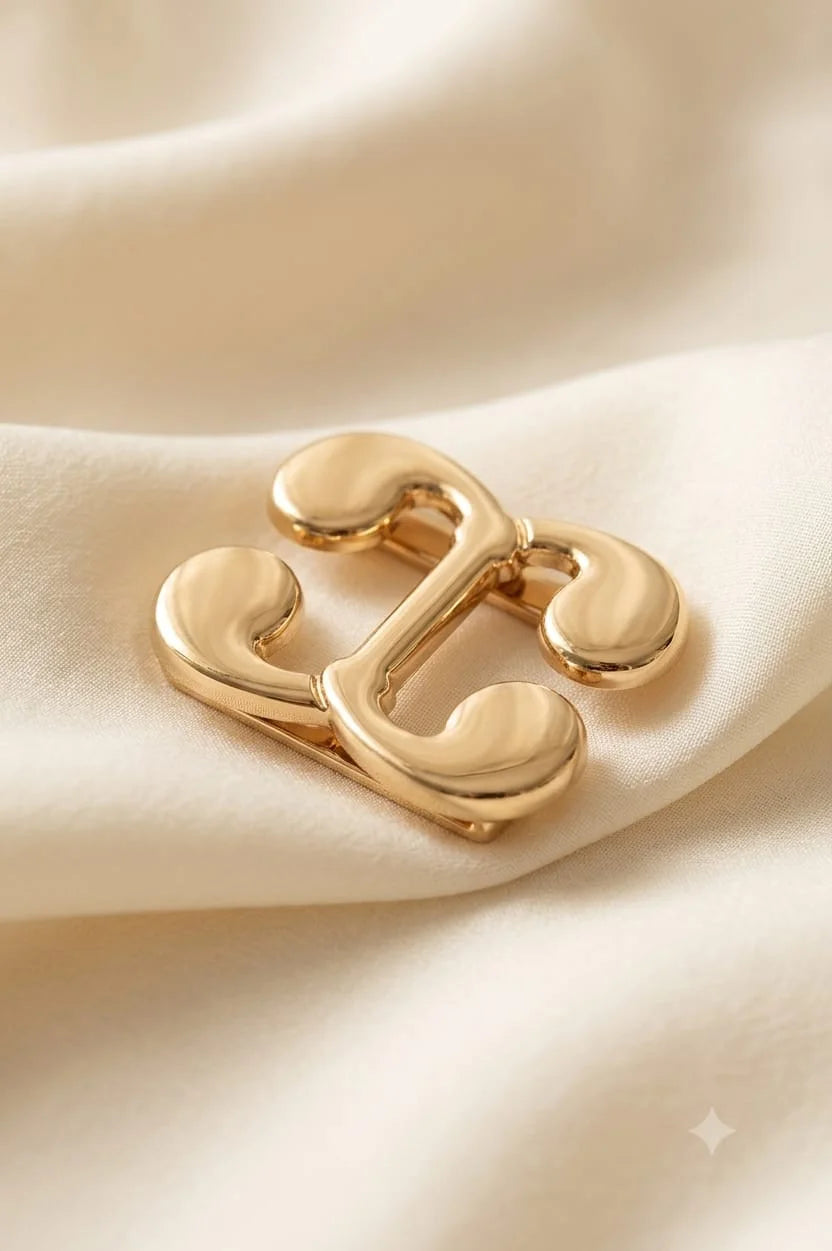 Sculptural gold-tone stainless steel scarf and garment clip displayed on cream satin fabric