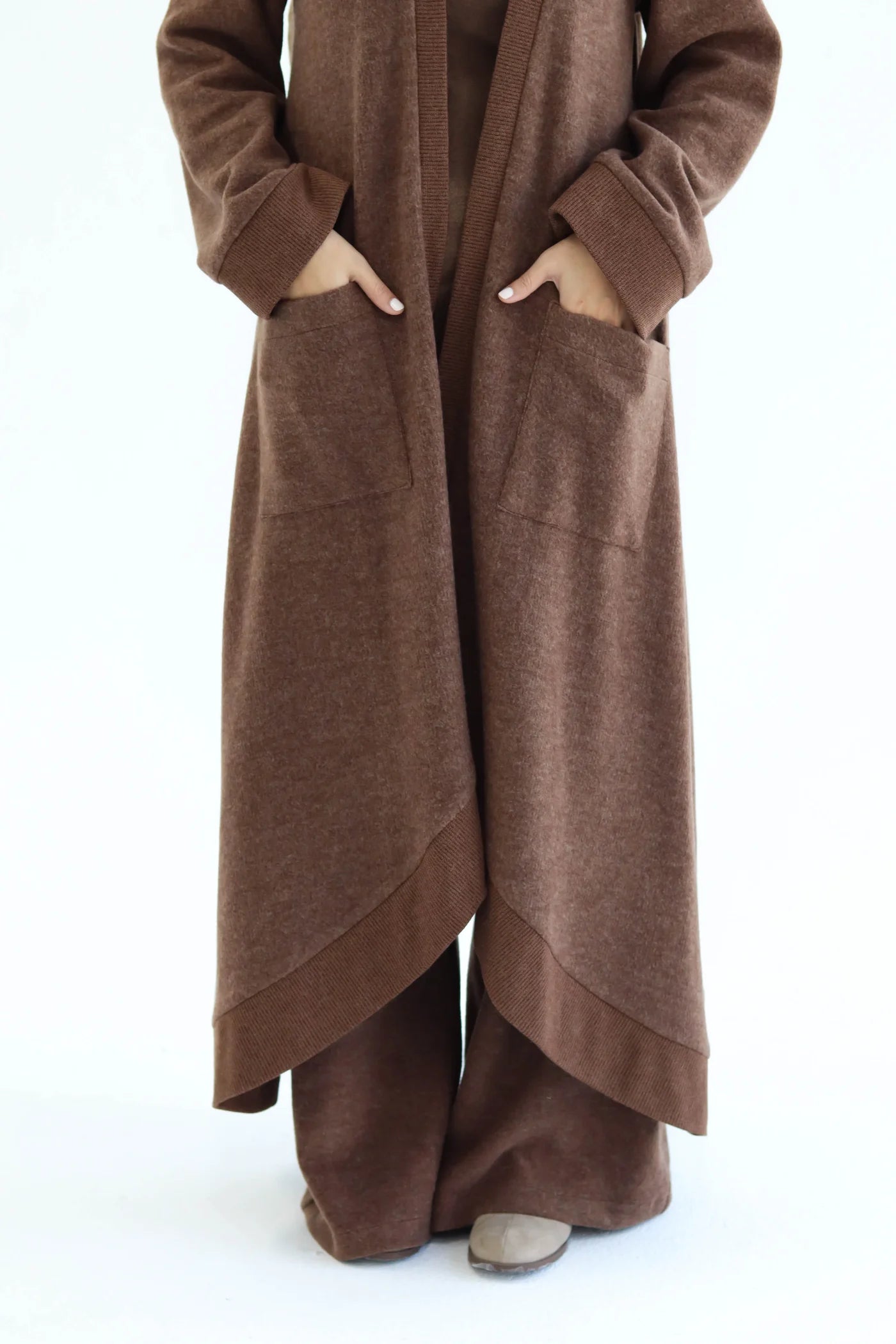 Brown knitted cardigan set detail showing layered hem, open front, and wide pants from knee level.