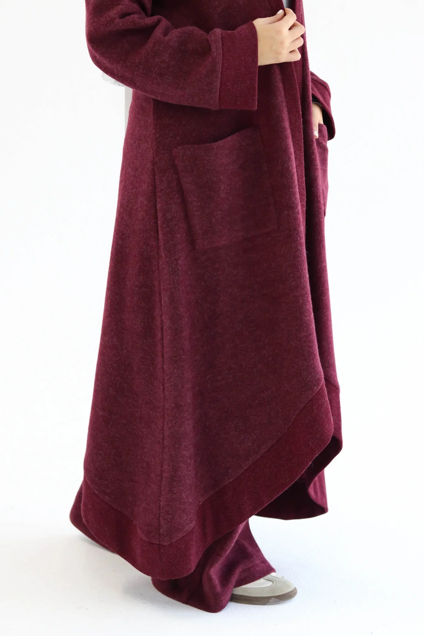 Close-up of burgundy knitted cardigan fabric showing texture, drape, and clean edge finish.