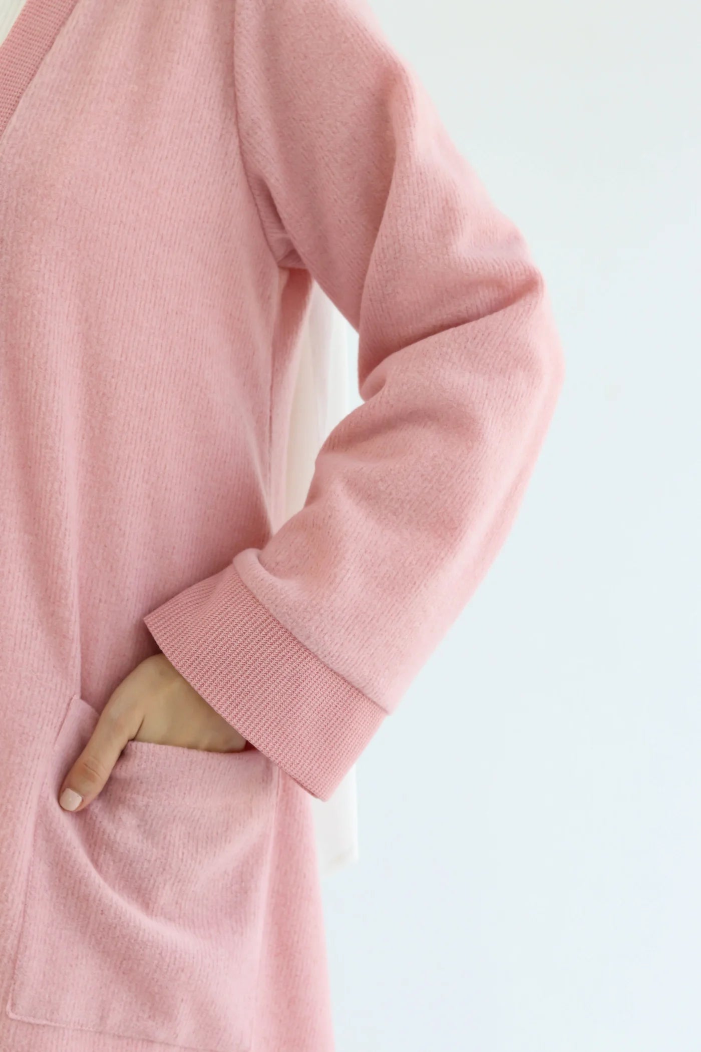 Pink knitted cardigan set close-up showing long sleeve, soft knit texture, and side pocket detail.