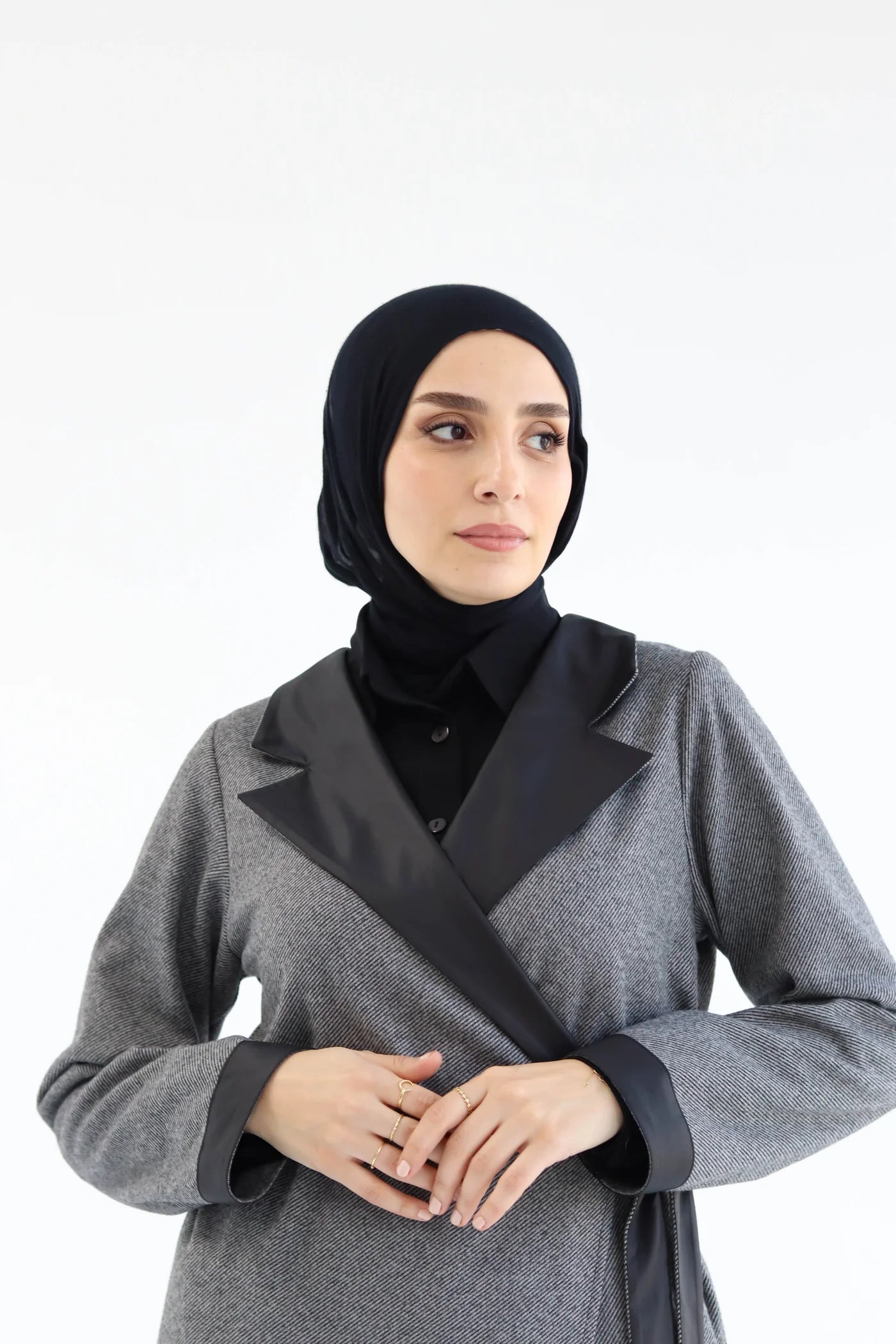 Woman wearing a gray coat with black trim and a black hijab on a white background