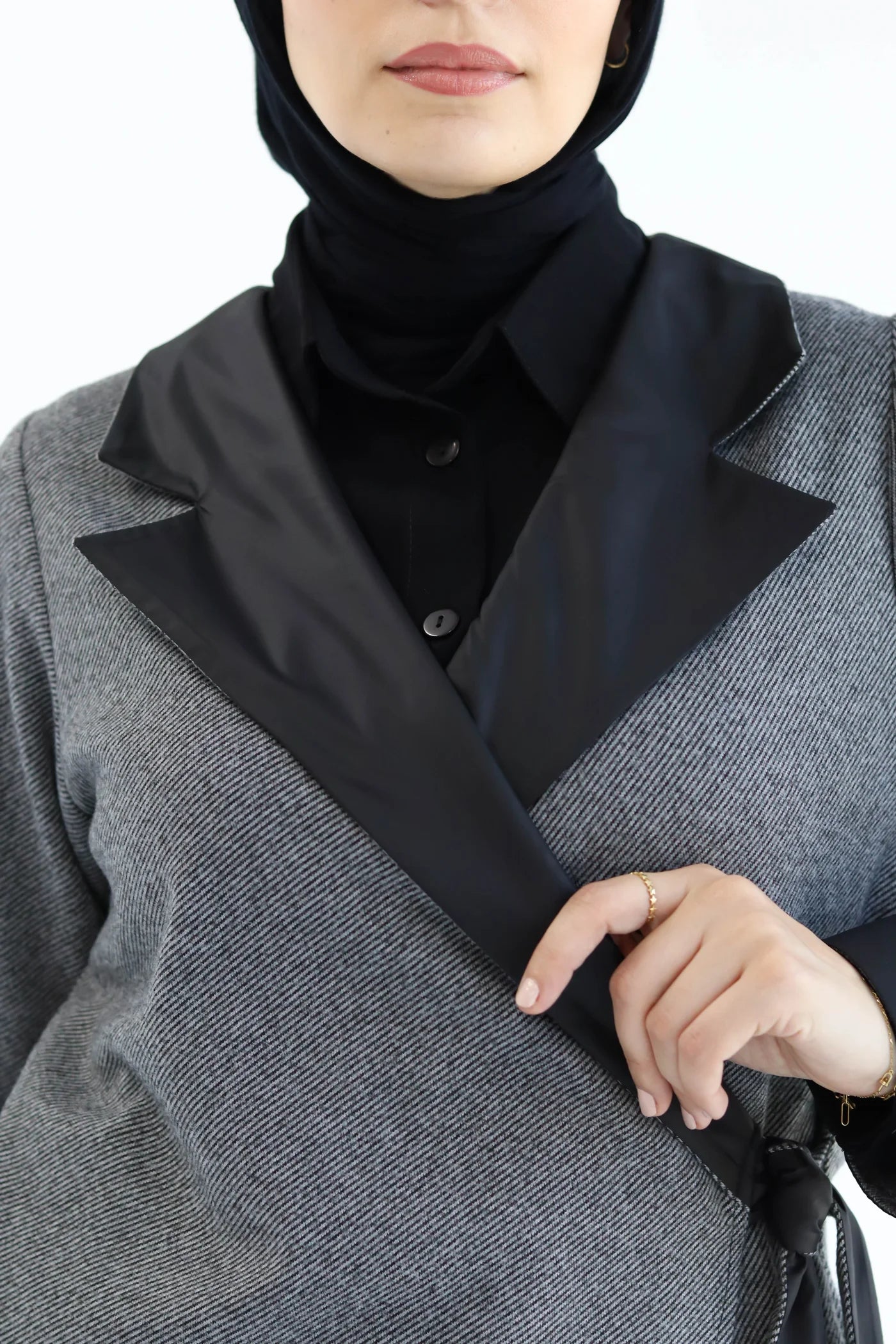Person wearing a gray wrap cardiganwith black lapels and a black hijab on a white background
