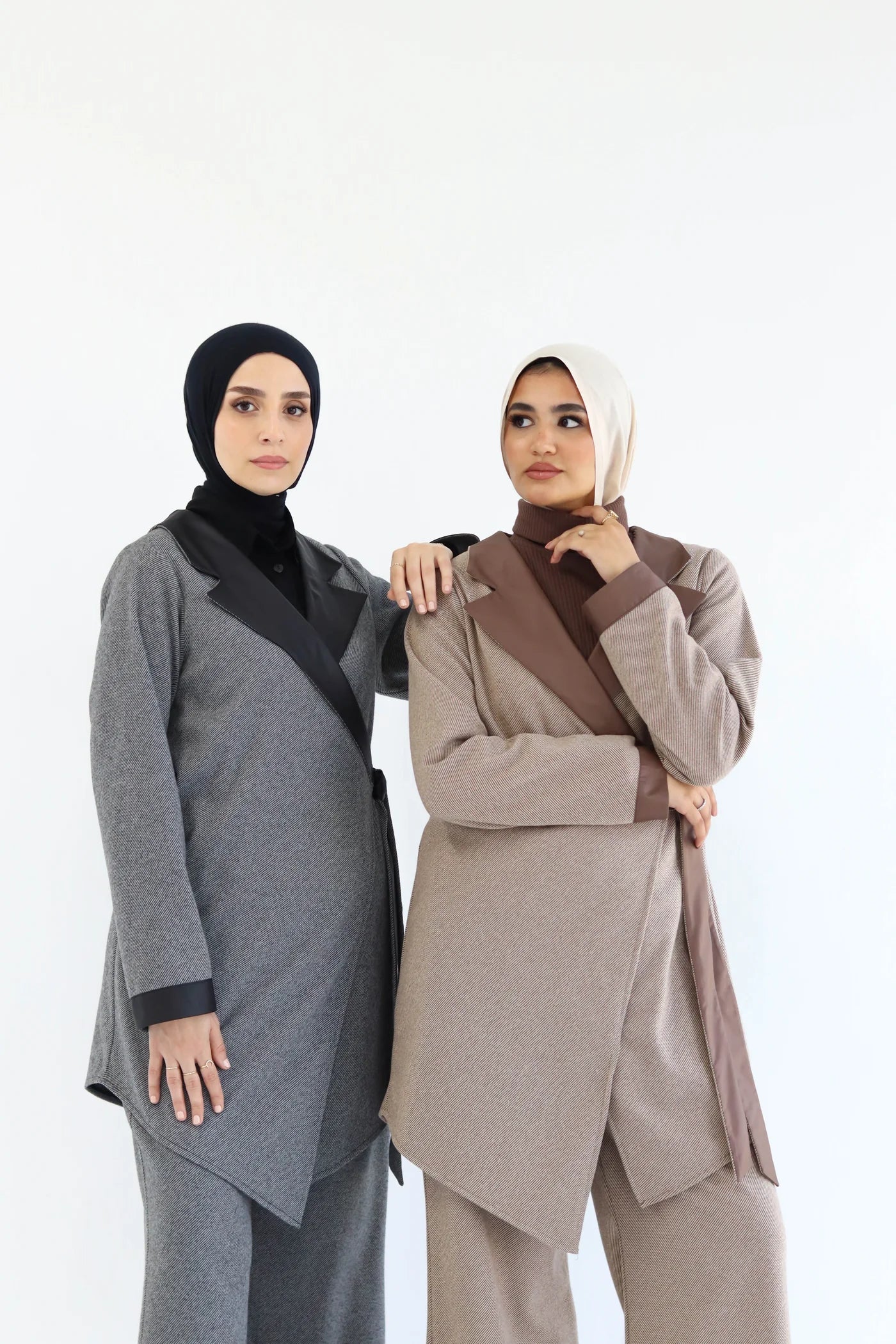 Two women wearing hijabs and long cardigans on a white background