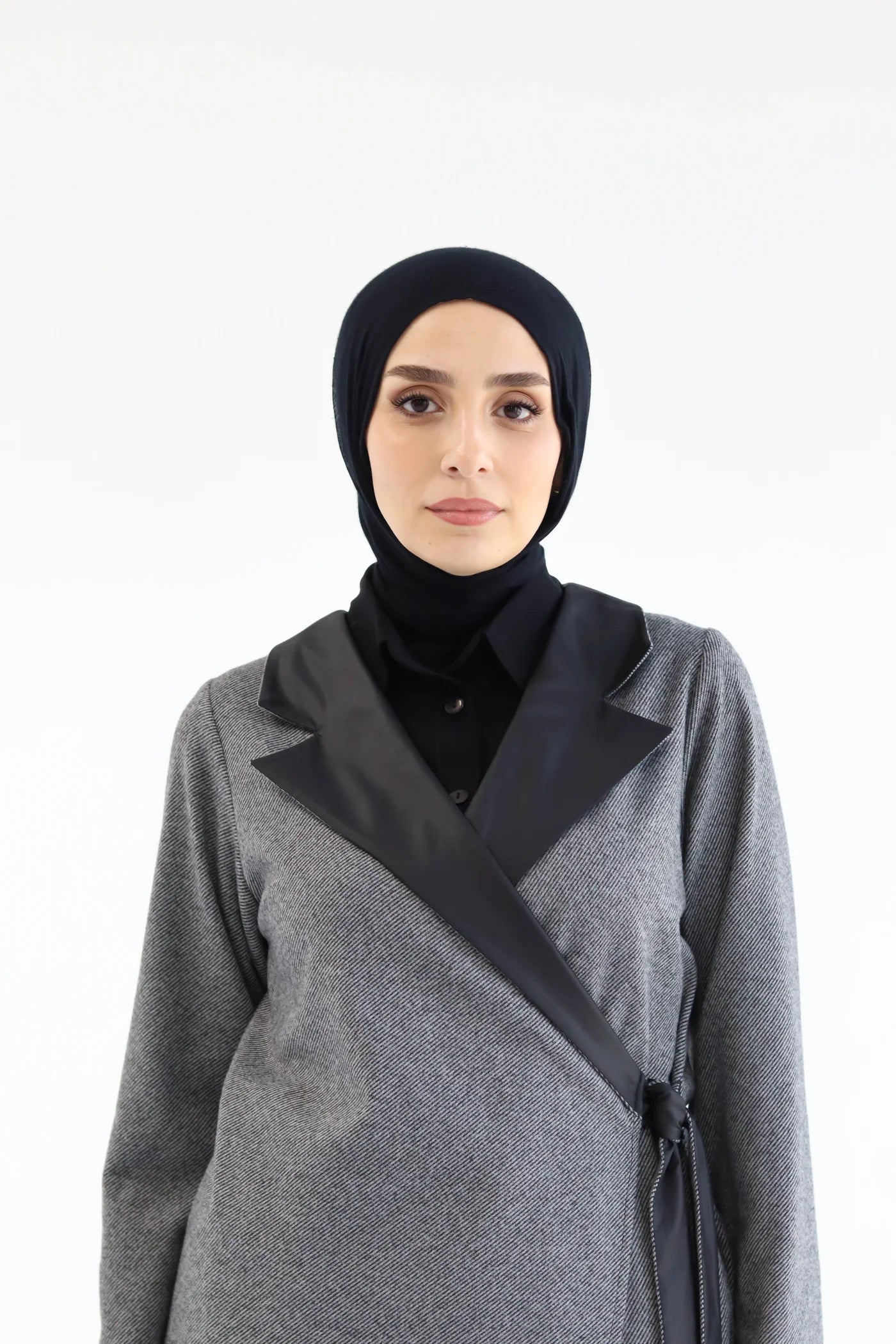 Woman wearing a gray cardigan with black trim and a black hijab on a white background