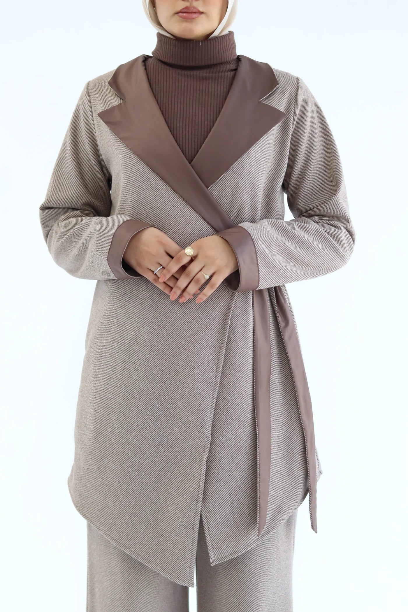 Person wearing a cafe cardigan with a brown belt and turtleneck on a white background