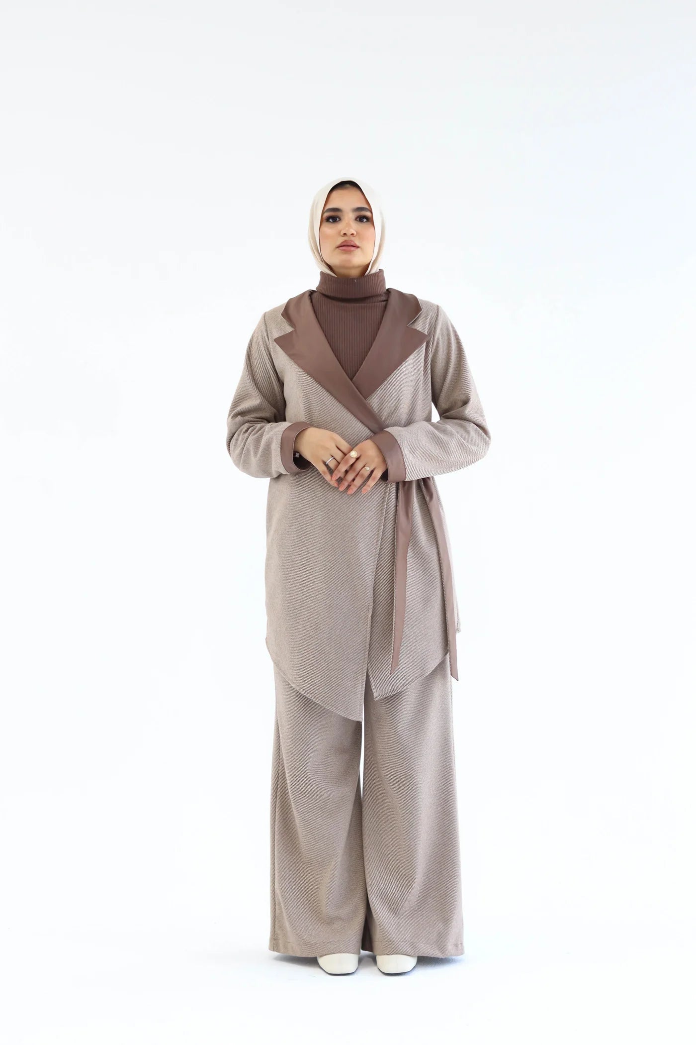 Woman wearing a beige outfit with a brown hijab on a white background