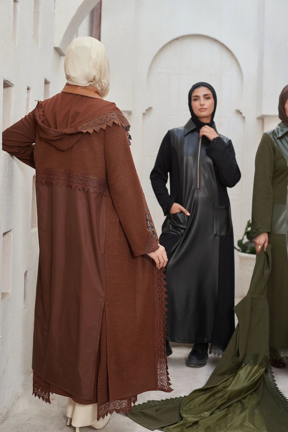 Three women wearing  Long knit guipure cardigan with leather details for modest winter layering and hijabs in front of a white architectural background