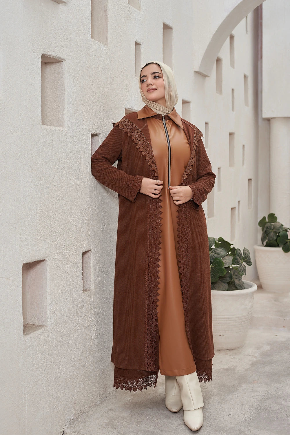 Woman wearing a  brown Long knit guipure cardigan with leather details for modest winter layering with lace details against a light-colored wall.
