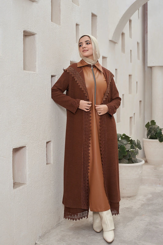 Woman wearing a  brown Long knit guipure cardigan with leather details for modest winter layering with lace details against a light-colored wall.