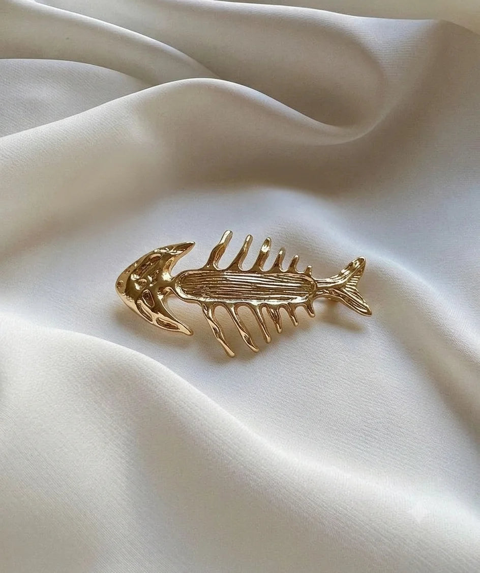 Gold-tone fish skeleton brooch on ivory fabric