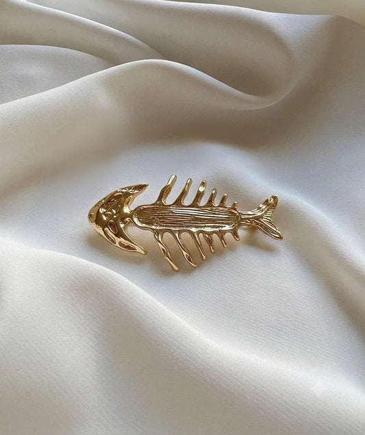 Gold-tone fish skeleton brooch on ivory fabric