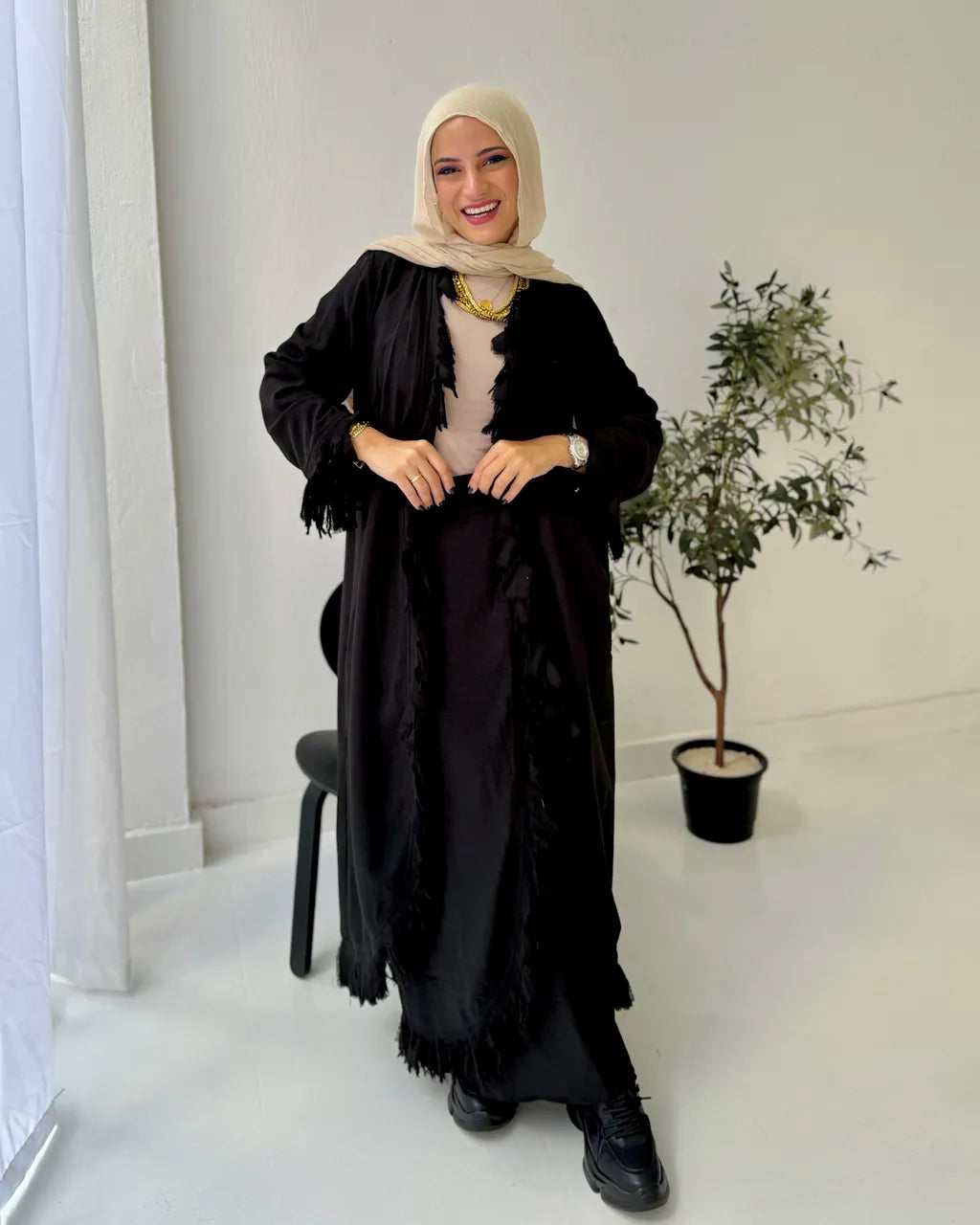 Woman wearing a black set with a hijab in a minimalistic room.