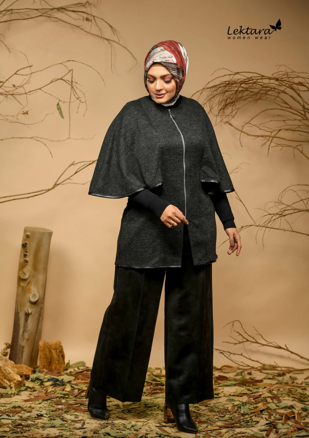 Woman wearing a Navy poncho and black pants with a patterned headscarf, standing against a natural background.